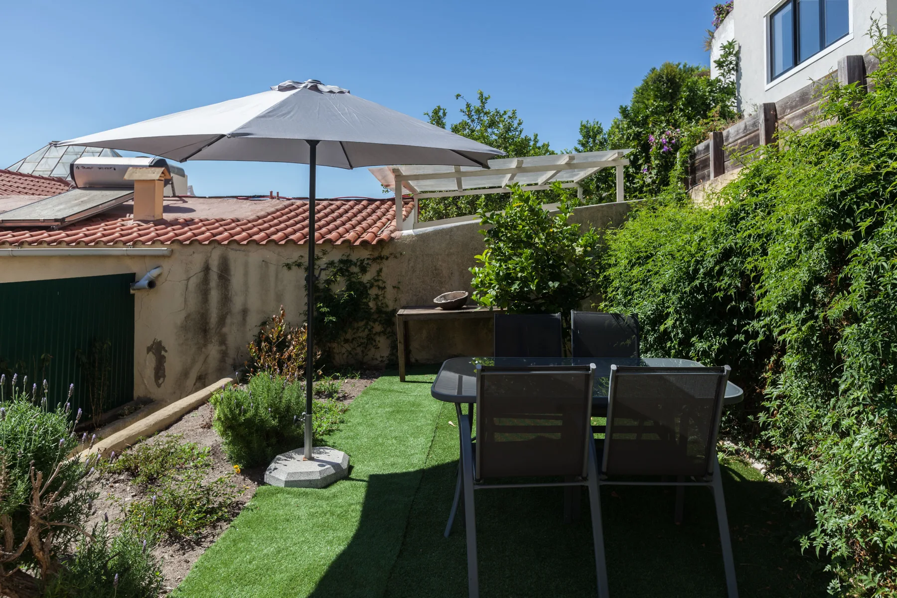 Una terraza al aire libre con una mesa, asientos y una sombrilla grande.