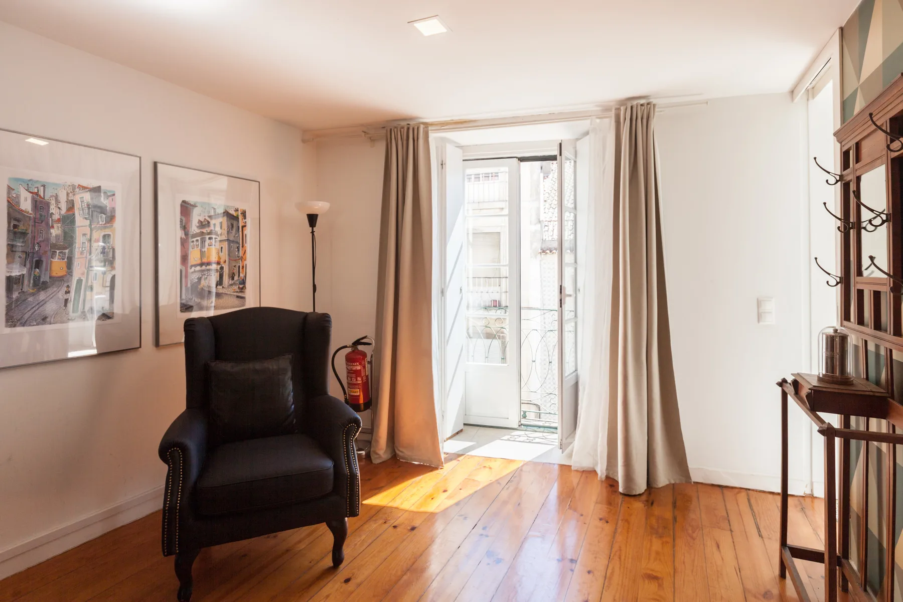 Una sala luminosa con un sillón junto a una puerta abierta al balcón.