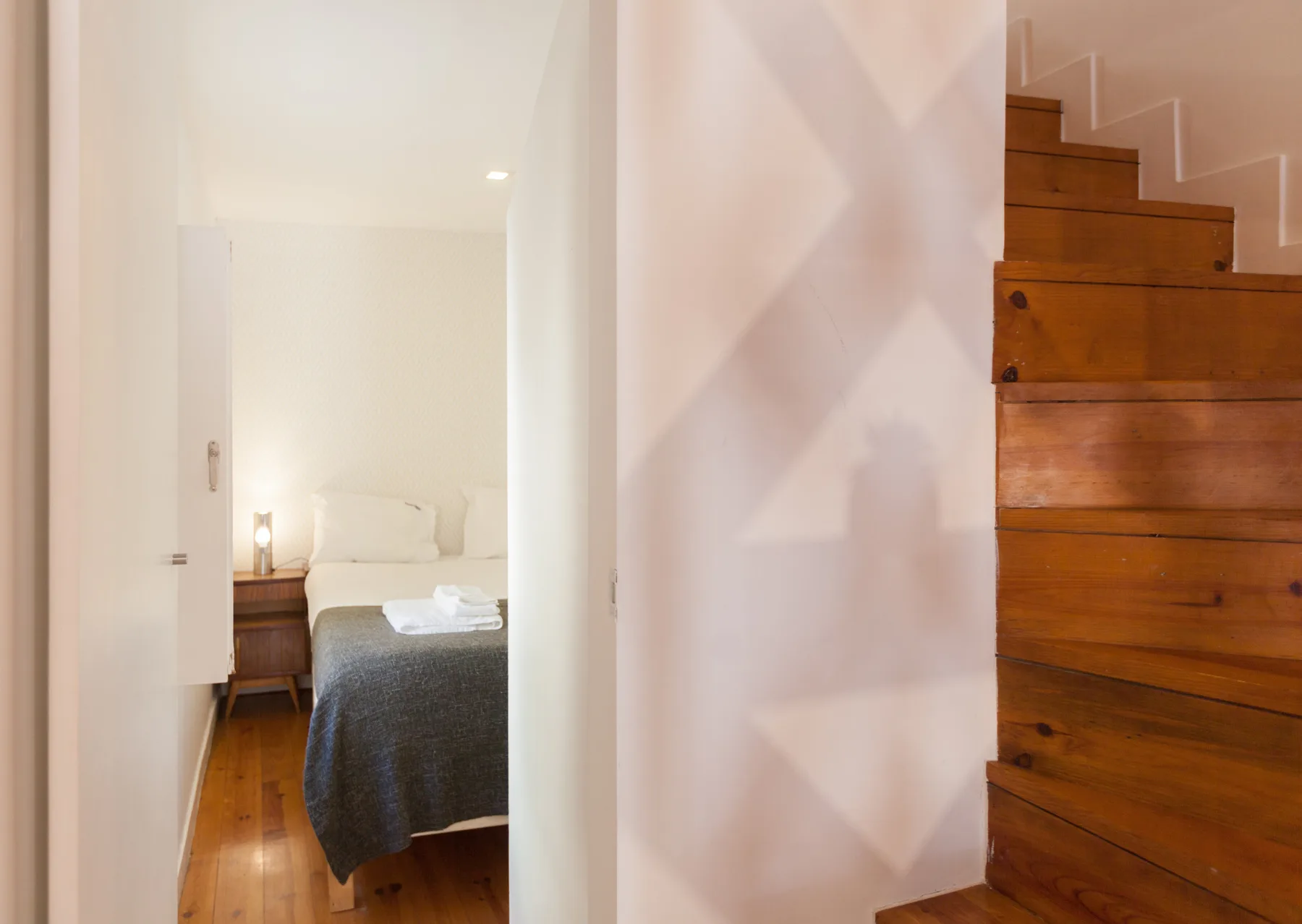 Un pasillo estrecho da a un dormitorio junto a una escalera de madera.