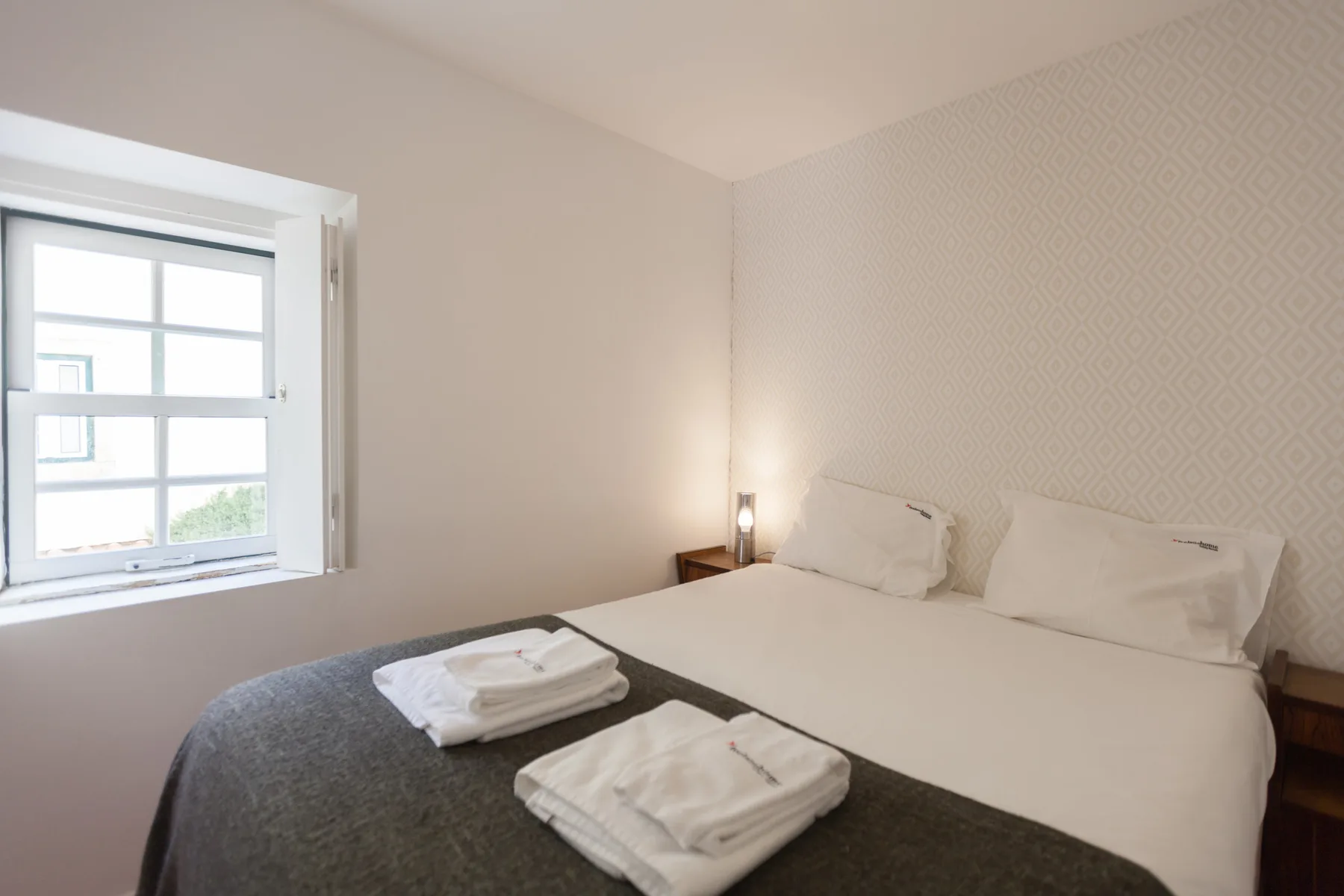 Dormitorio con una cama y una ventana con vistas a edificios cercanos.