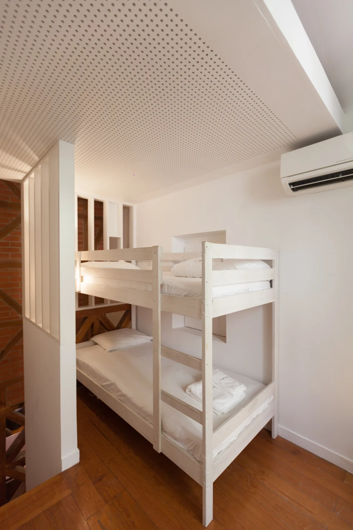 Un dormitorio con literas blancas y un aire acondicionado en la pared.