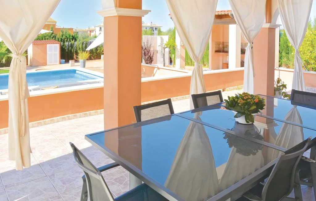 Una zona de comedor exterior cubierta da a una piscina.