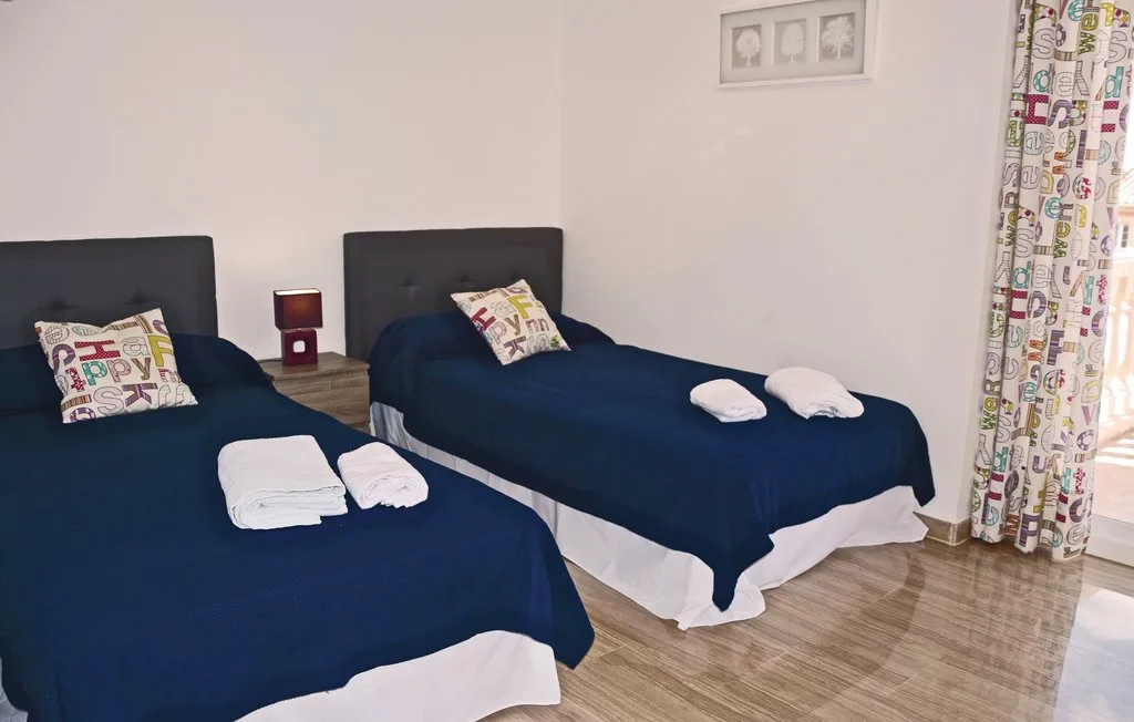 Un dormitorio con dos camas cubiertas con ropa de cama azul oscuro y toallas dobladas.