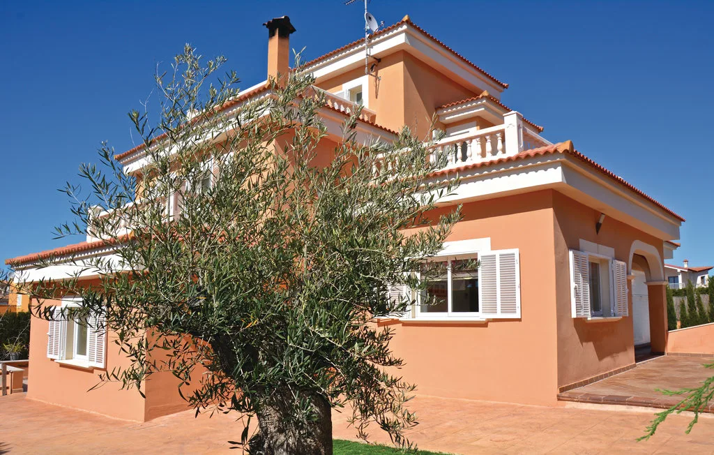 Una casa color melocotón con ventanas de marco blanco está junto a un árbol frondoso.
