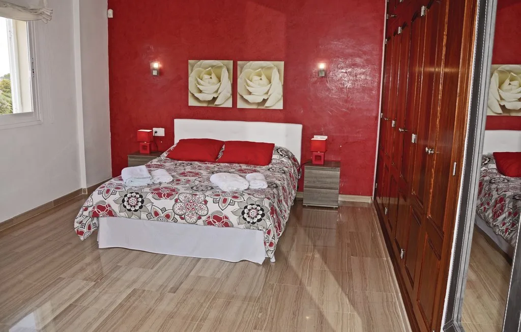 Un dormitorio con una cama, una pared roja y un armario con espejo.