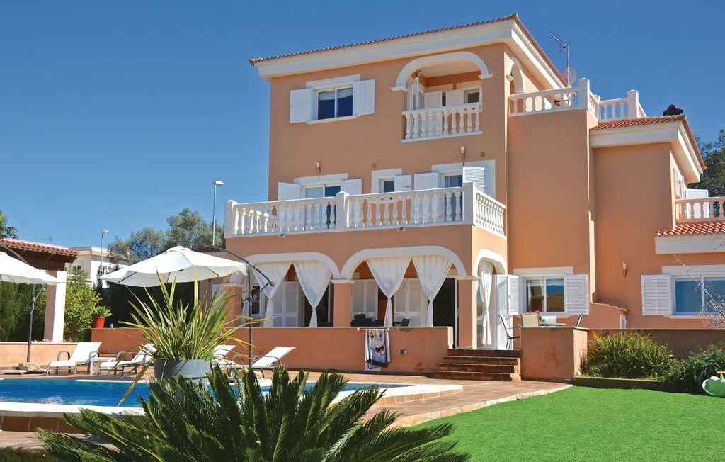 Una casa color melocotón está junto a una piscina y un césped verde.