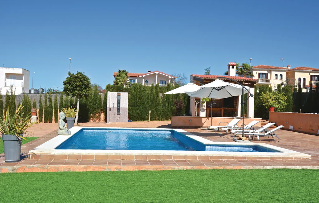 Una piscina exterior está junto a un patio con asientos reclinables y una sombrilla.