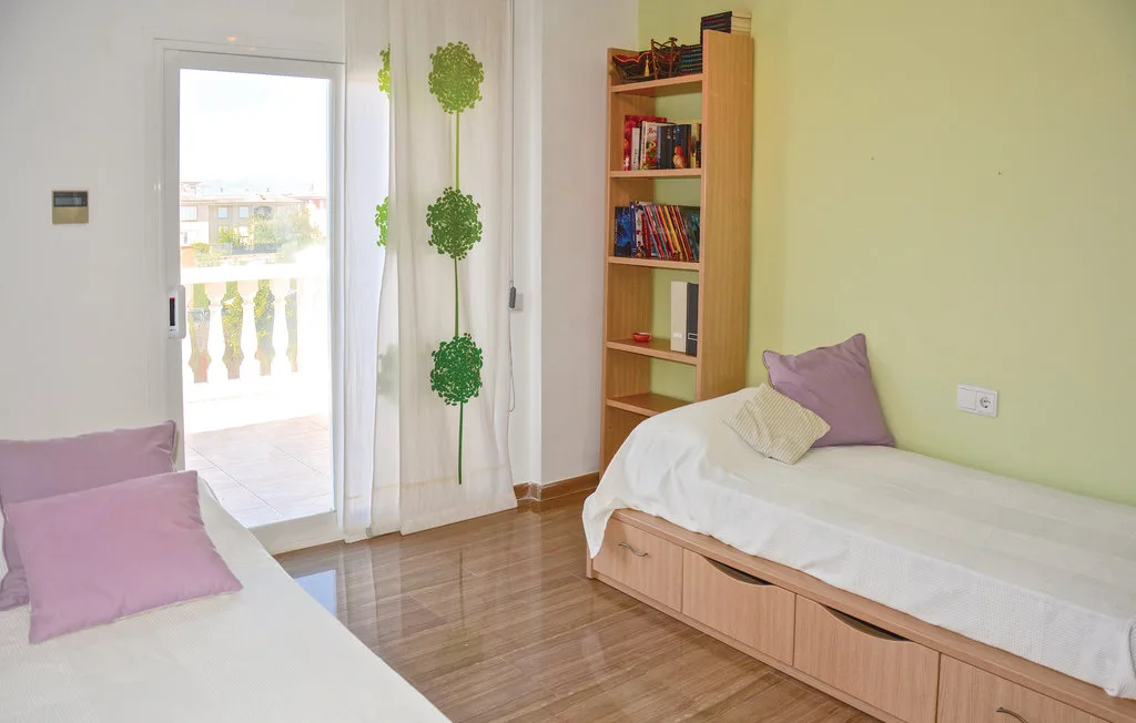 Un dormitorio con dos camas individuales, una estantería y una puerta luminosa al balcón.