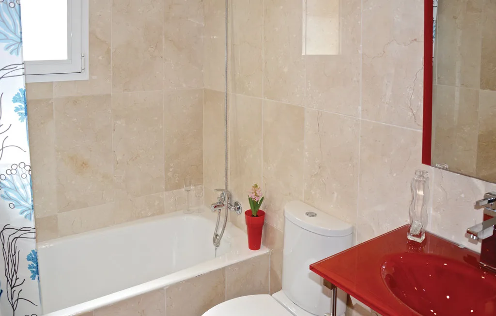 Baño alicatado con bañera, inodoro y encimera roja con lavabo.