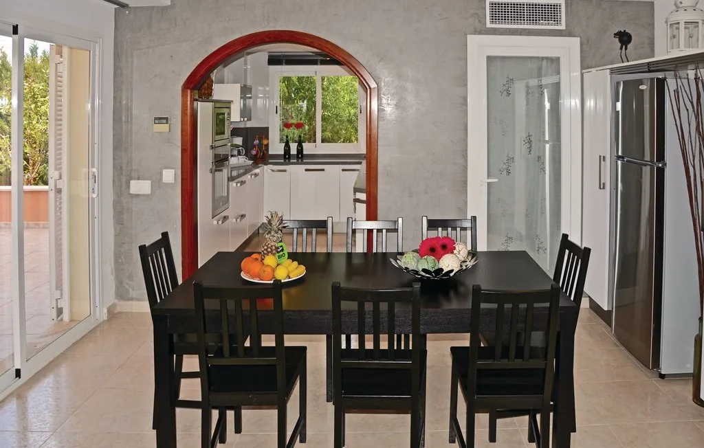 Comedor con una mesa oscura y sillas junto a una cocina abierta.