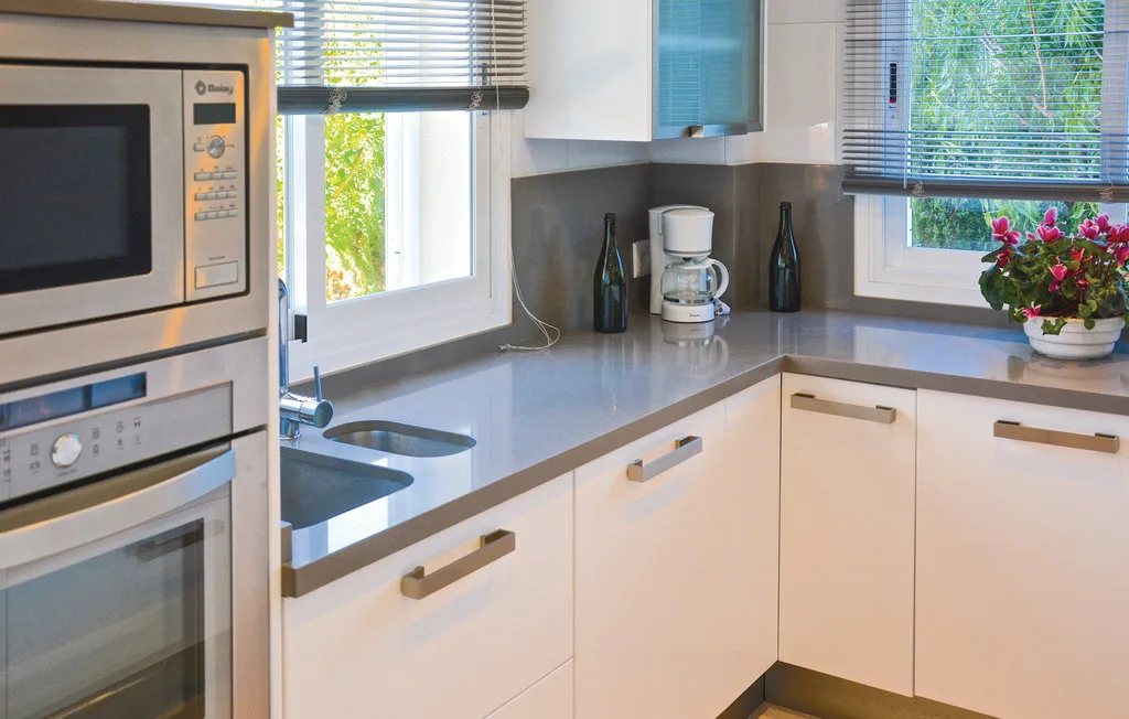 Una cocina moderna y luminosa con gabinetes claros, electrodomésticos empotrados y una encimera esquinera.