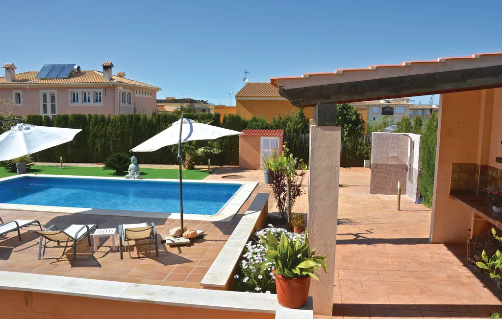 Una piscina al aire libre junto a un patio de baldosas con asientos y sombrillas blancas.