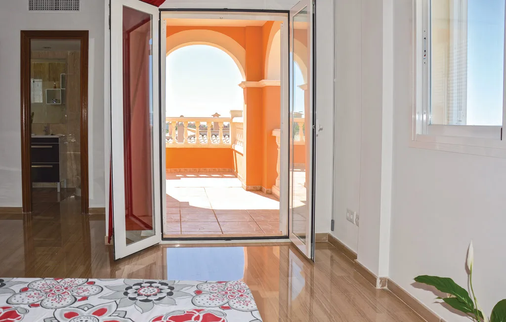 Una habitación luminosa da a un balcón naranja con arcos, a través de puertas de vidrio abiertas.