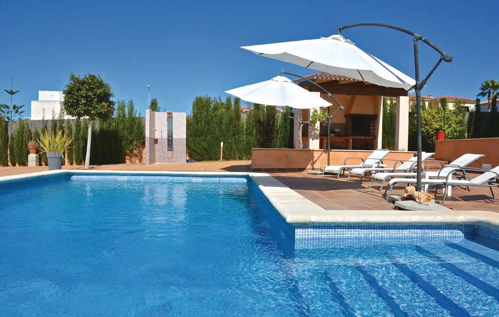 Zona junto a la piscina con asientos reclinables y sombrillas blancas.