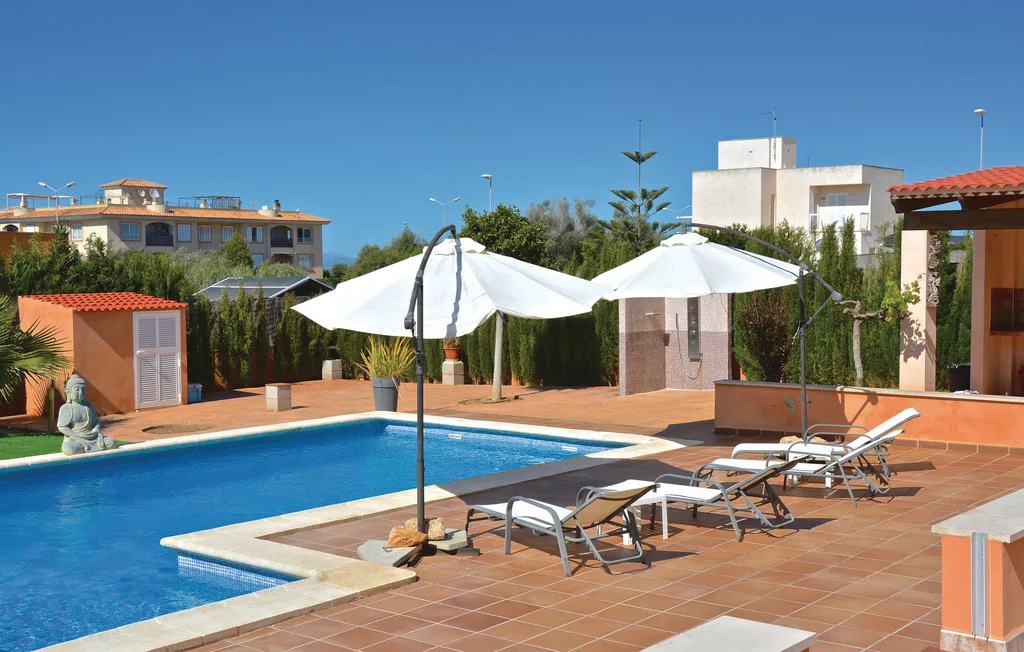 Una piscina al aire libre junto a un patio de baldosas con tumbonas y sombrillas.