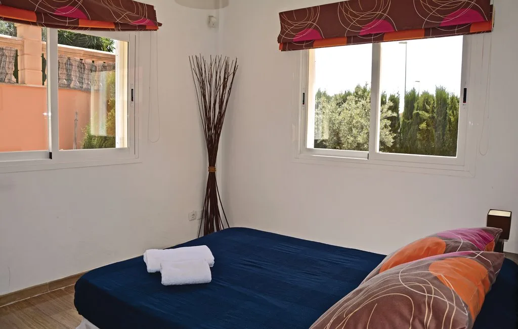 Un dormitorio con una cama, una toalla doblada y dos ventanas.