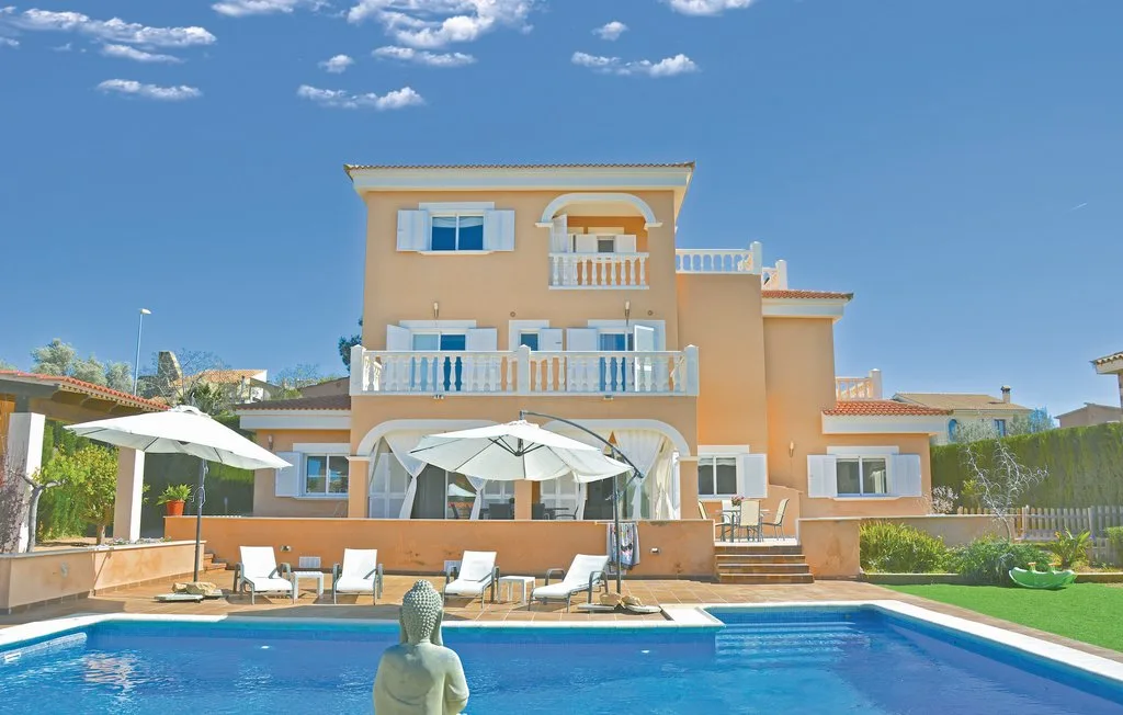 Una casa de varios pisos da a una piscina con asientos y sombrillas.