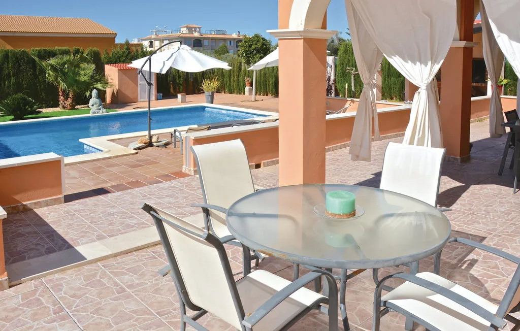 Un patio exterior embaldosado con una mesa de vidrio da a una piscina.