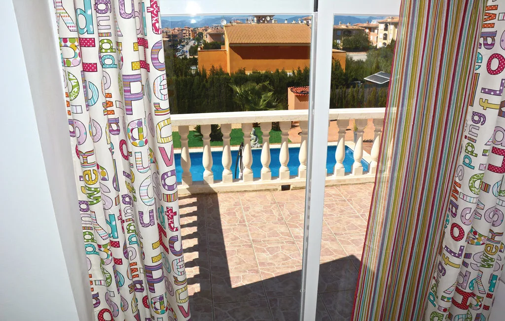 Una puerta de vidrio da a un balcón de baldosas con vistas a una piscina y edificios cercanos.