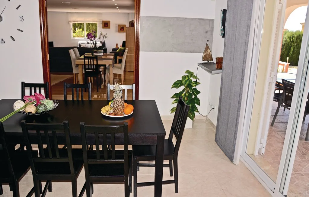 Un comedor con una mesa oscura y sillas junto a una puerta abierta al patio.