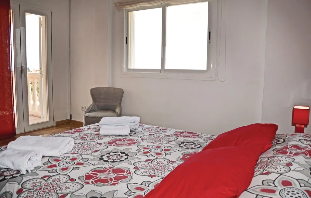 Un dormitorio con una colcha estampada, cojines rojos y una ventana.