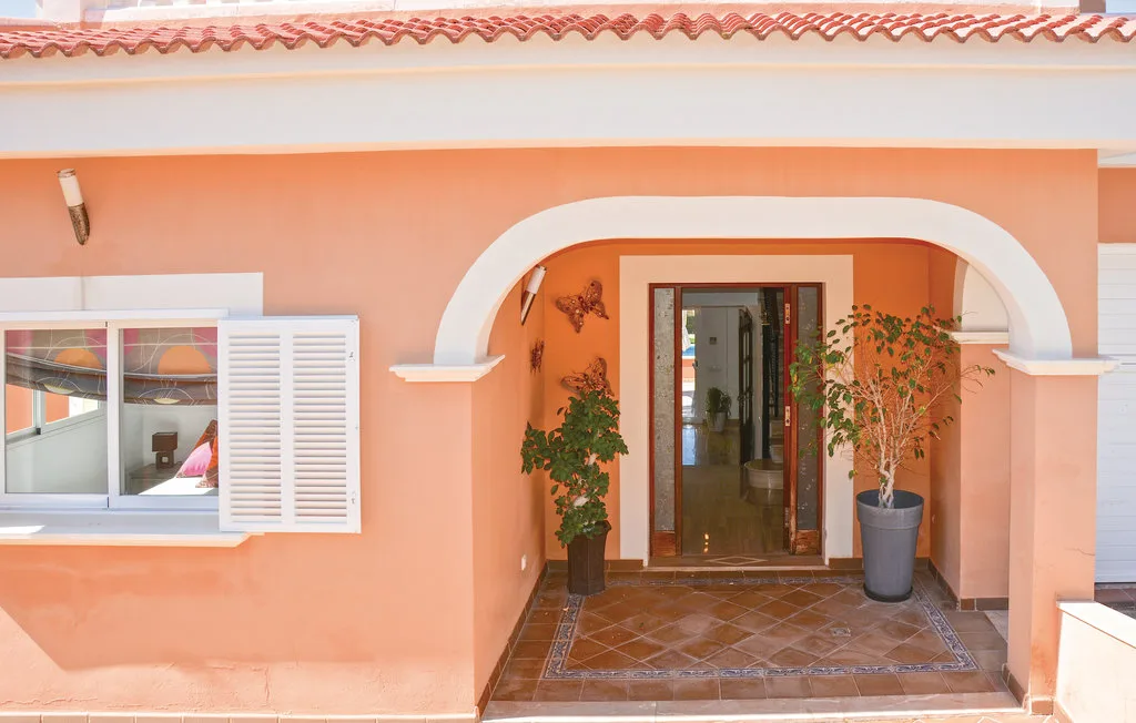 La entrada de una casa color durazno tiene un porche con arco y una puerta acristalada.