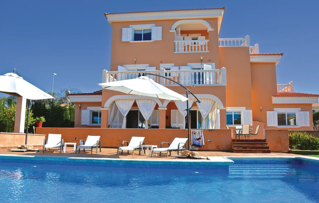 Una casa naranja de varias plantas se alza detrás de una piscina y asientos en el patio.