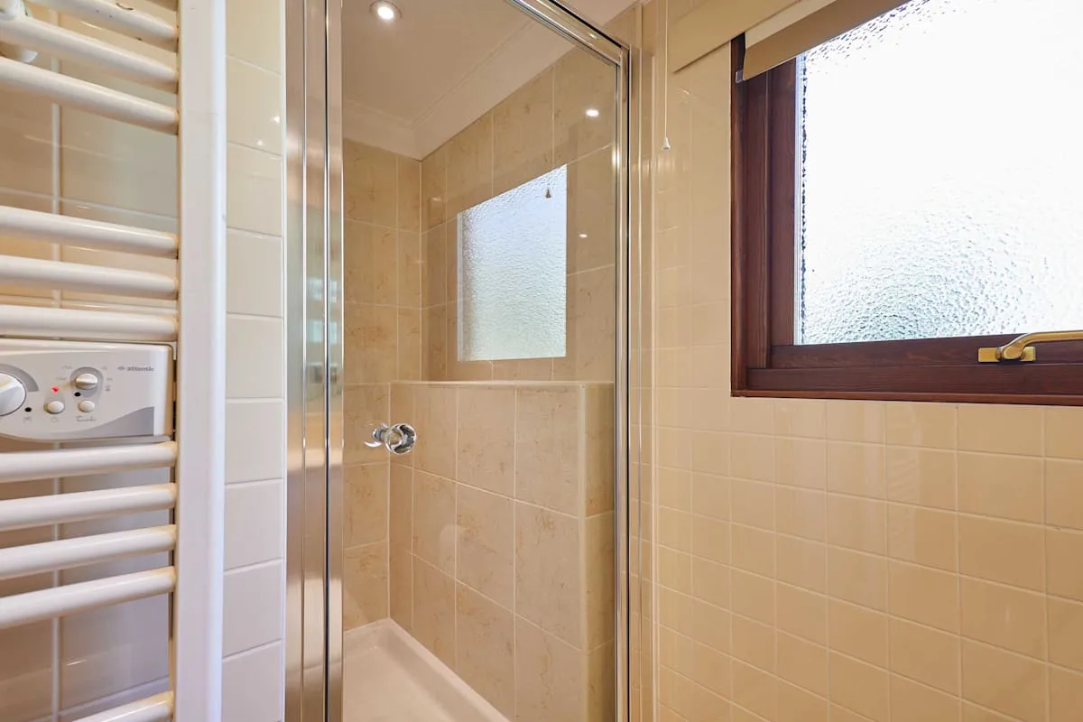 A tiled bathroom with a glass shower and a frosted window.