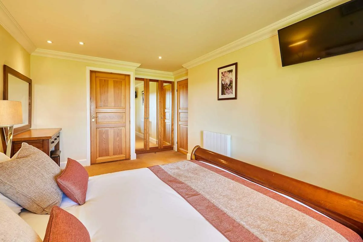 A bedroom with a bed, wooden doors, and a wall-mounted television.