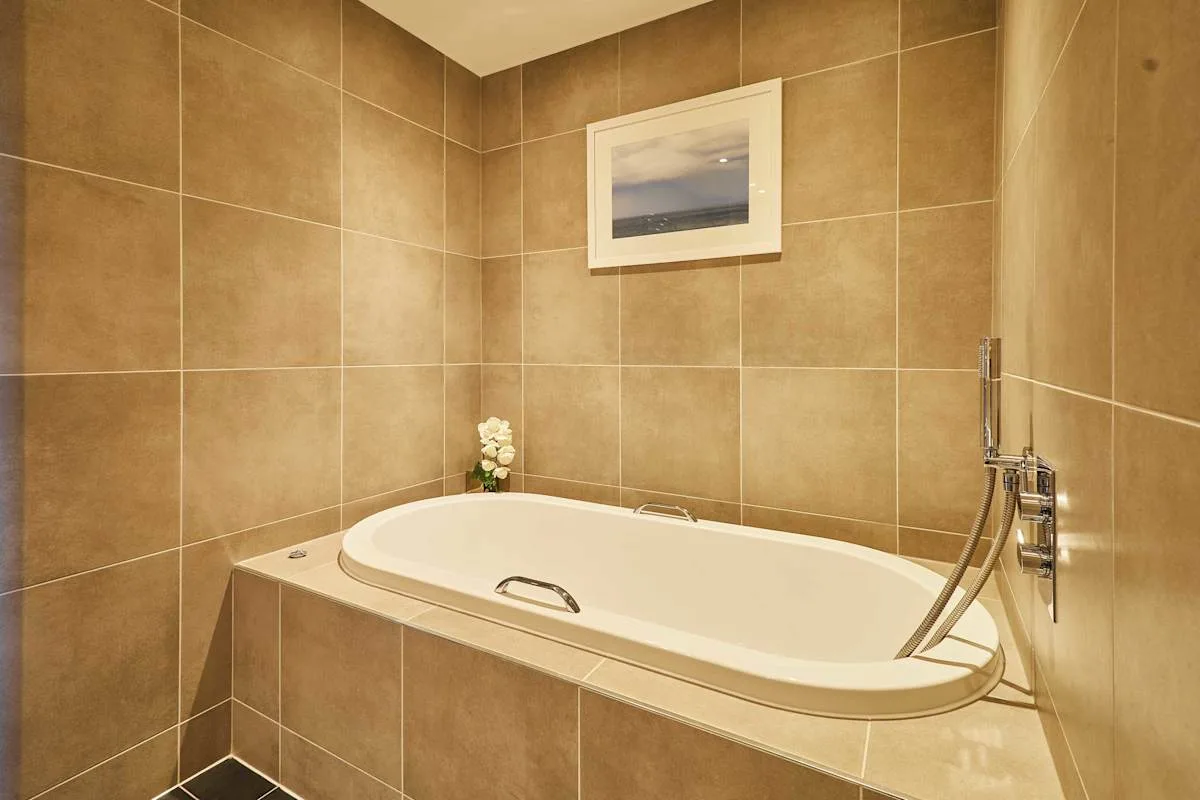 A tiled bathroom features a built-in bathtub and wall-mounted shower fixtures.