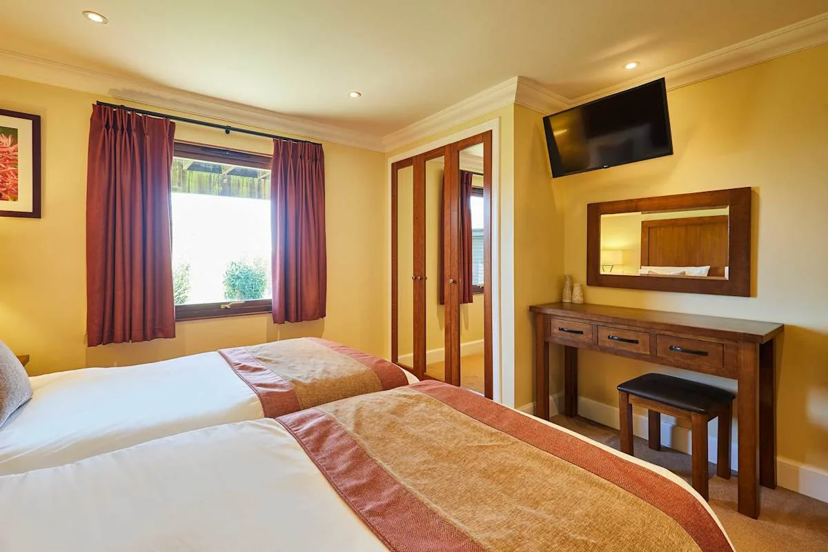 A bedroom with two beds, a window, and a desk with a mirror.