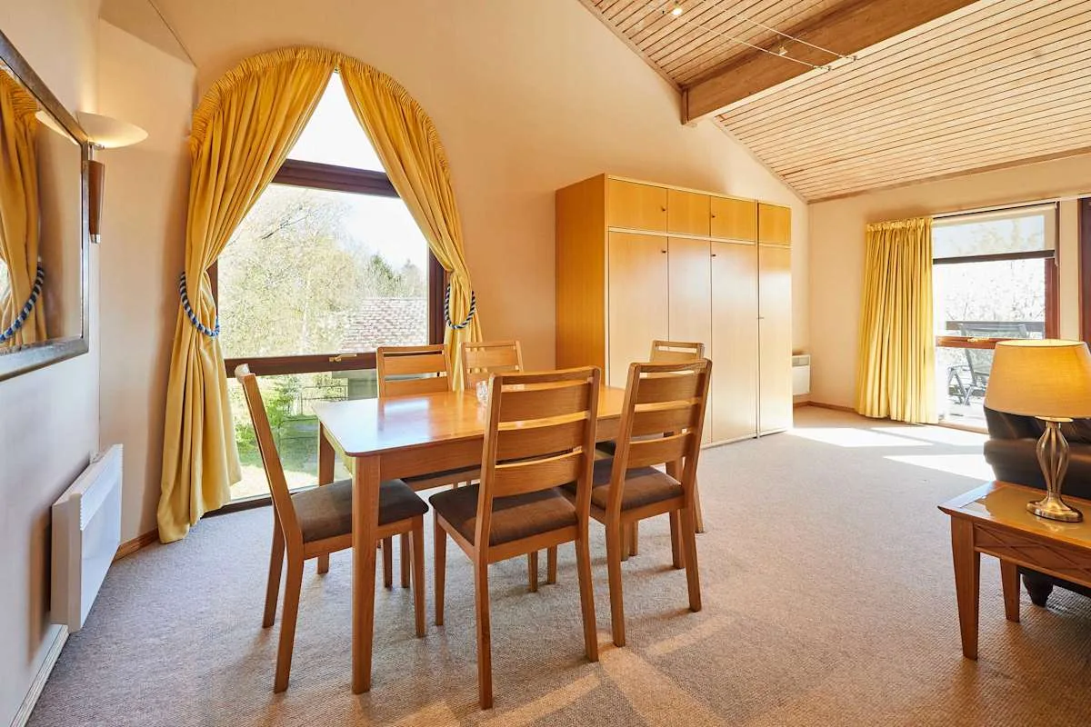 A dining area with a wooden table and chairs beside curtained windows.