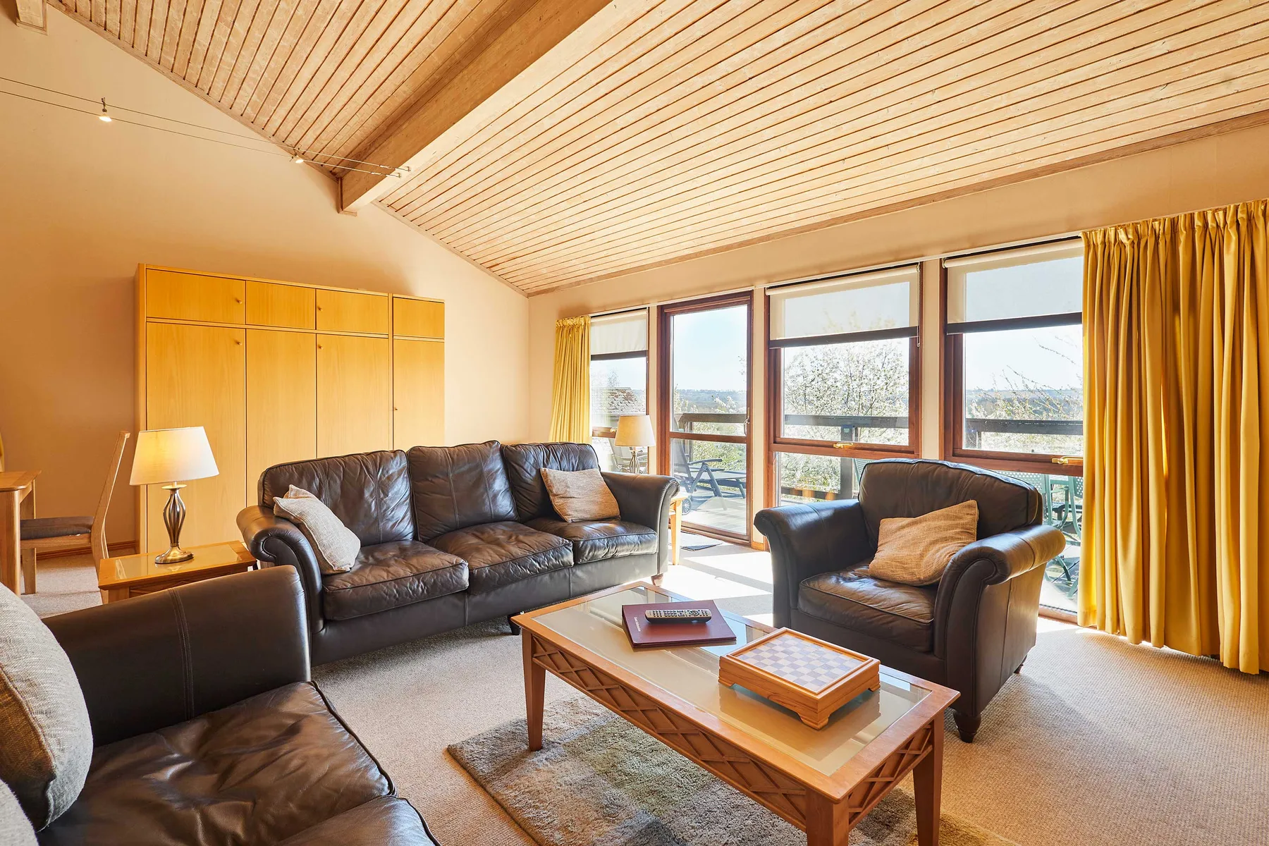 A living room with dark seating, a wooden coffee table, and large windows.