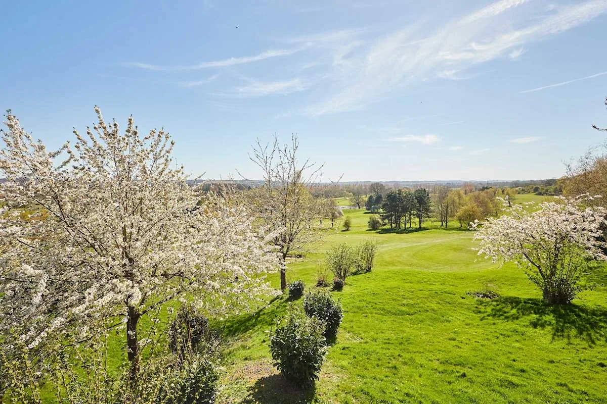 A green lawn bordered by flowering trees stretches toward the distant countryside.