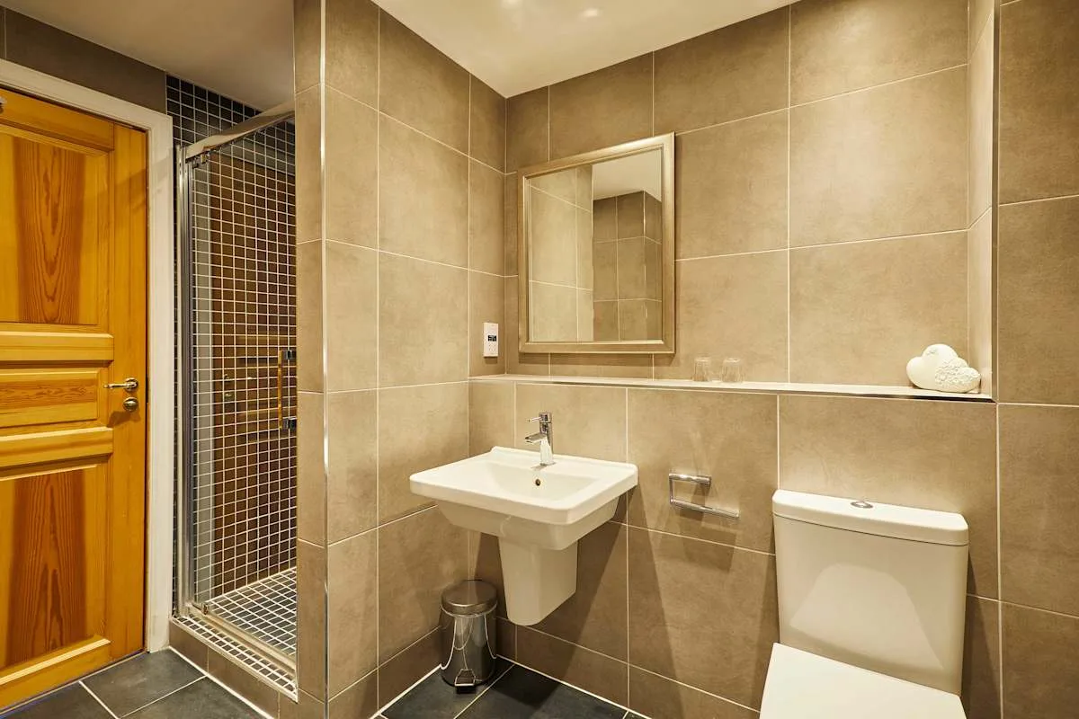 A tiled bathroom with a sink, mirror, toilet, and shower.