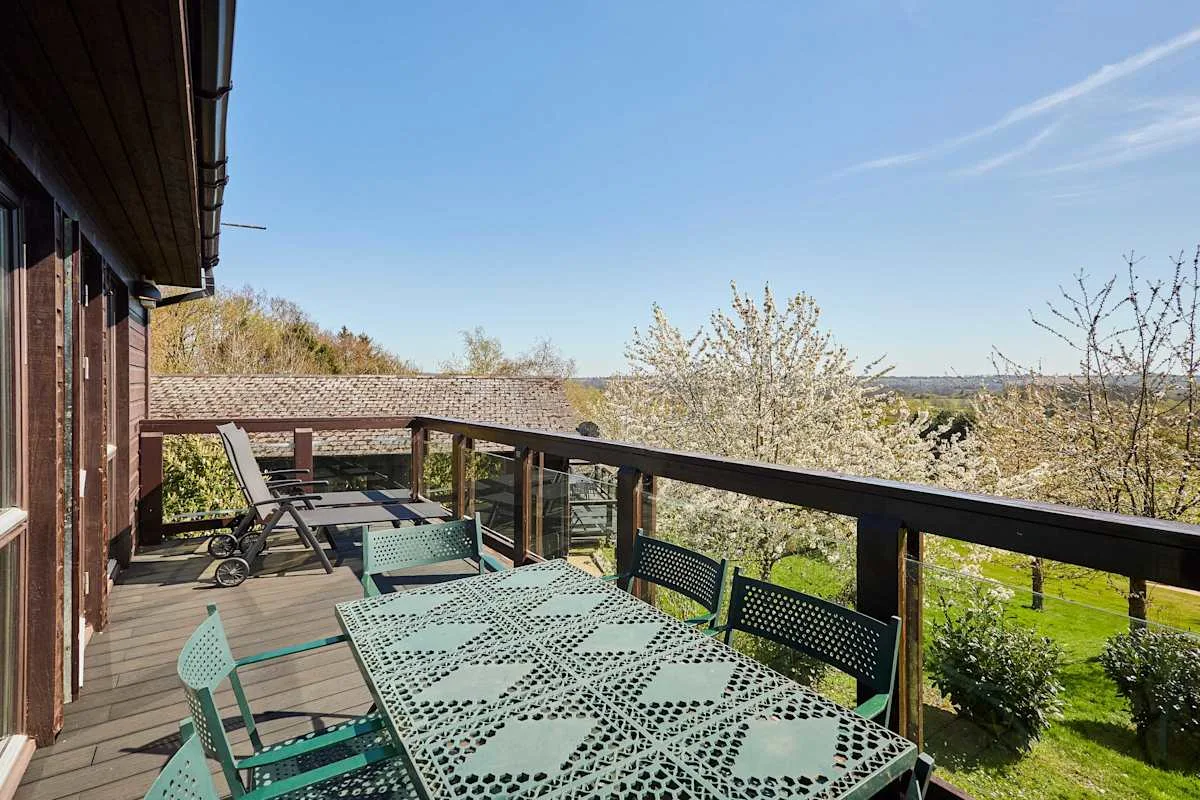A wooden deck with outdoor seating overlooks a garden and distant hills.