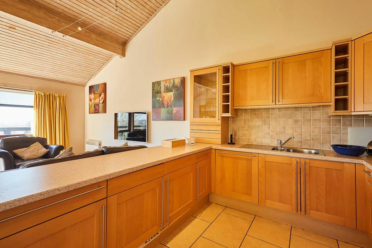 A kitchen with wooden cabinets and a counter overlooking a small seating area.