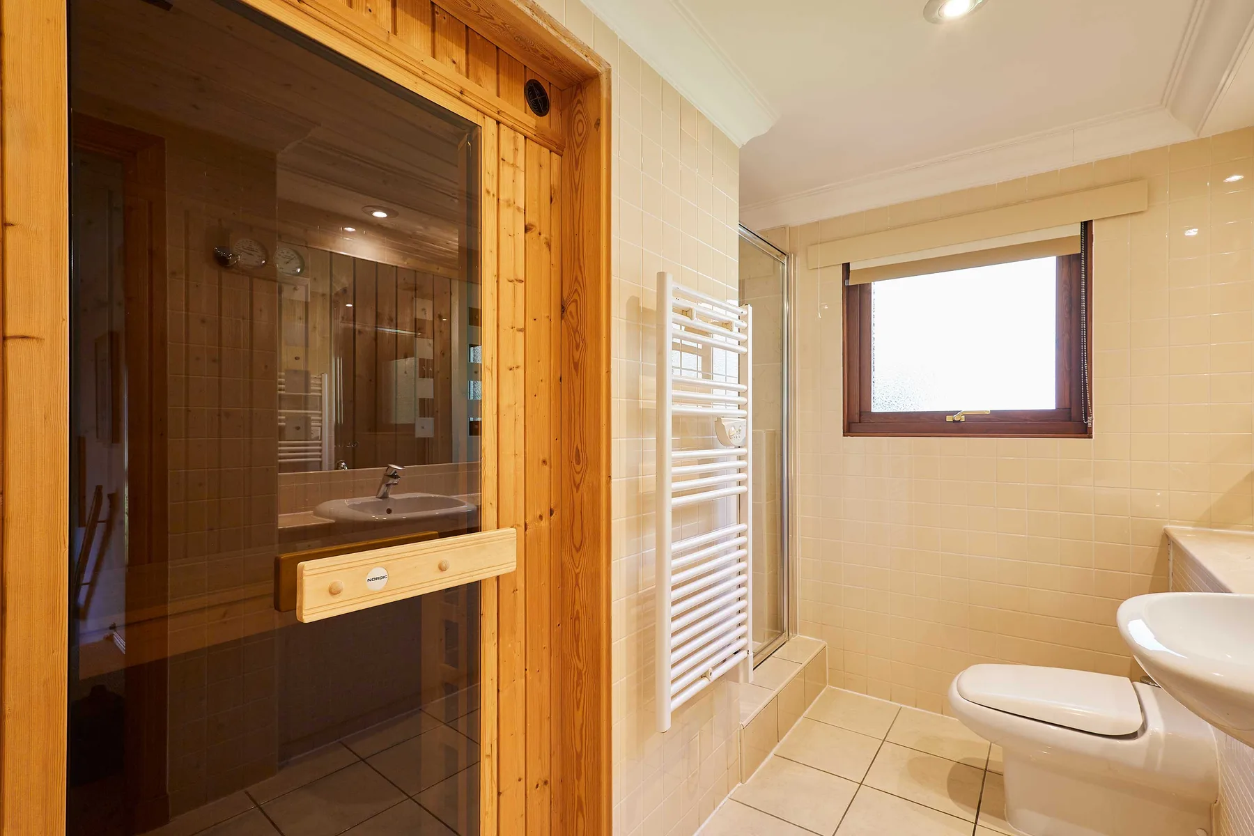 A tiled bathroom with a glass-fronted sauna and a window.
