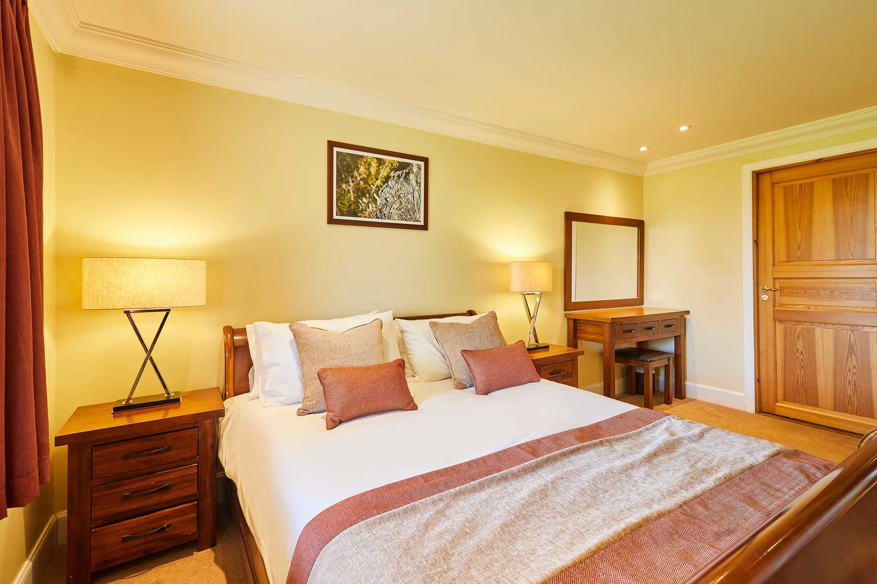 Bedroom with a neatly made bed, bedside tables, and a wooden door.