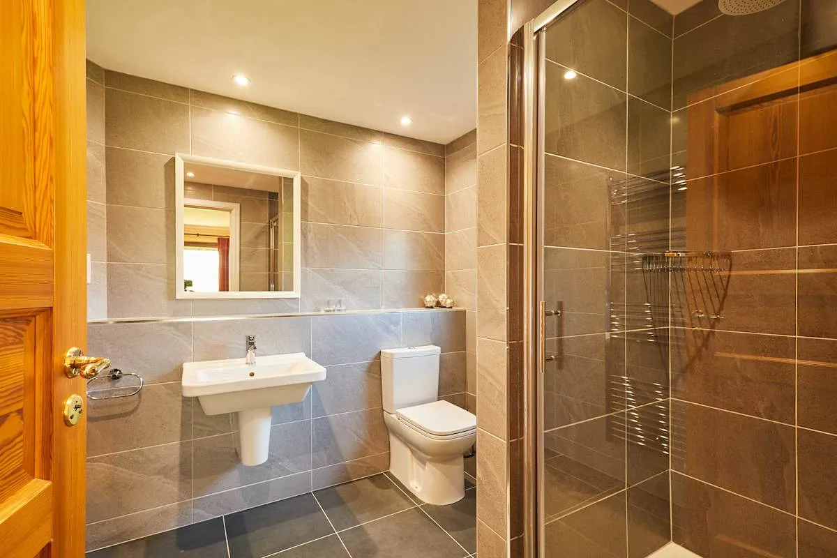 A tiled bathroom with a sink, mirror, toilet, and glass shower.