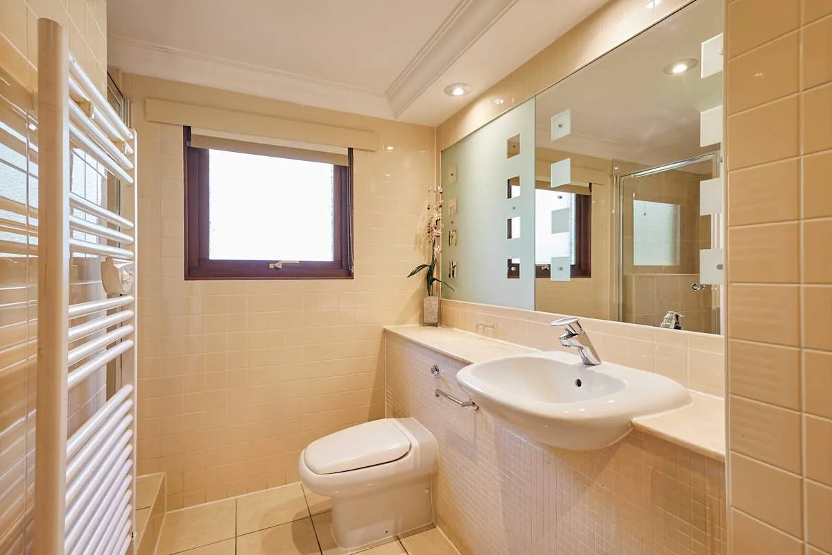 A tiled bathroom with a sink, toilet, and wall-mounted towel warmer.