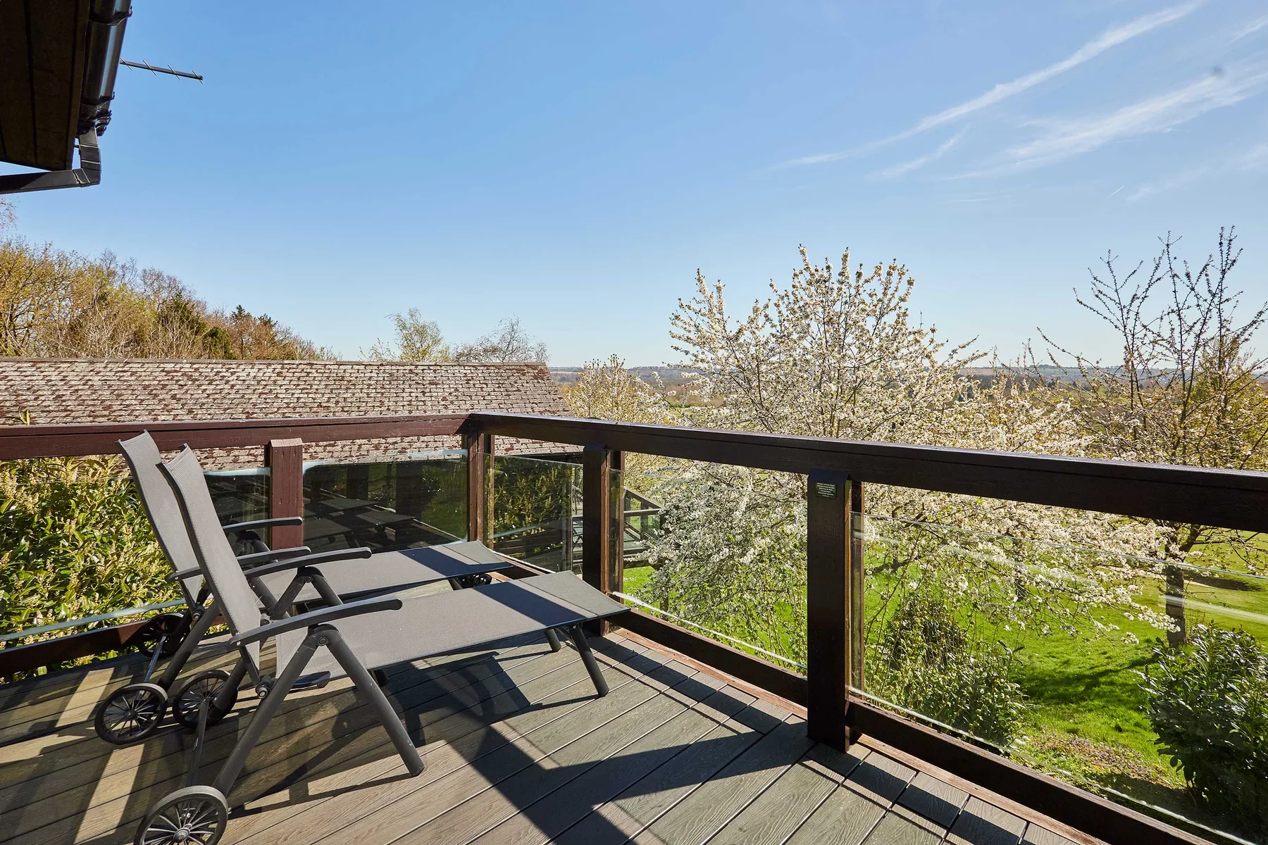 A wooden outdoor deck overlooks a green garden beneath a clear blue sky.