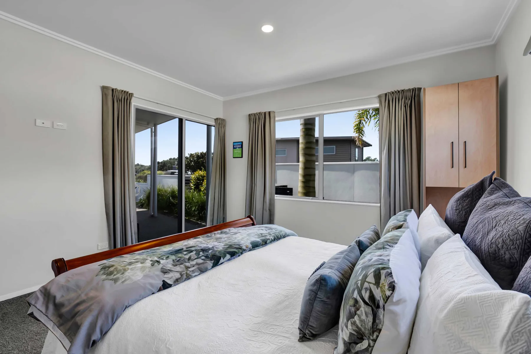 Un dormitorio luminoso con una cama, ventanas con cortinas y un armario.