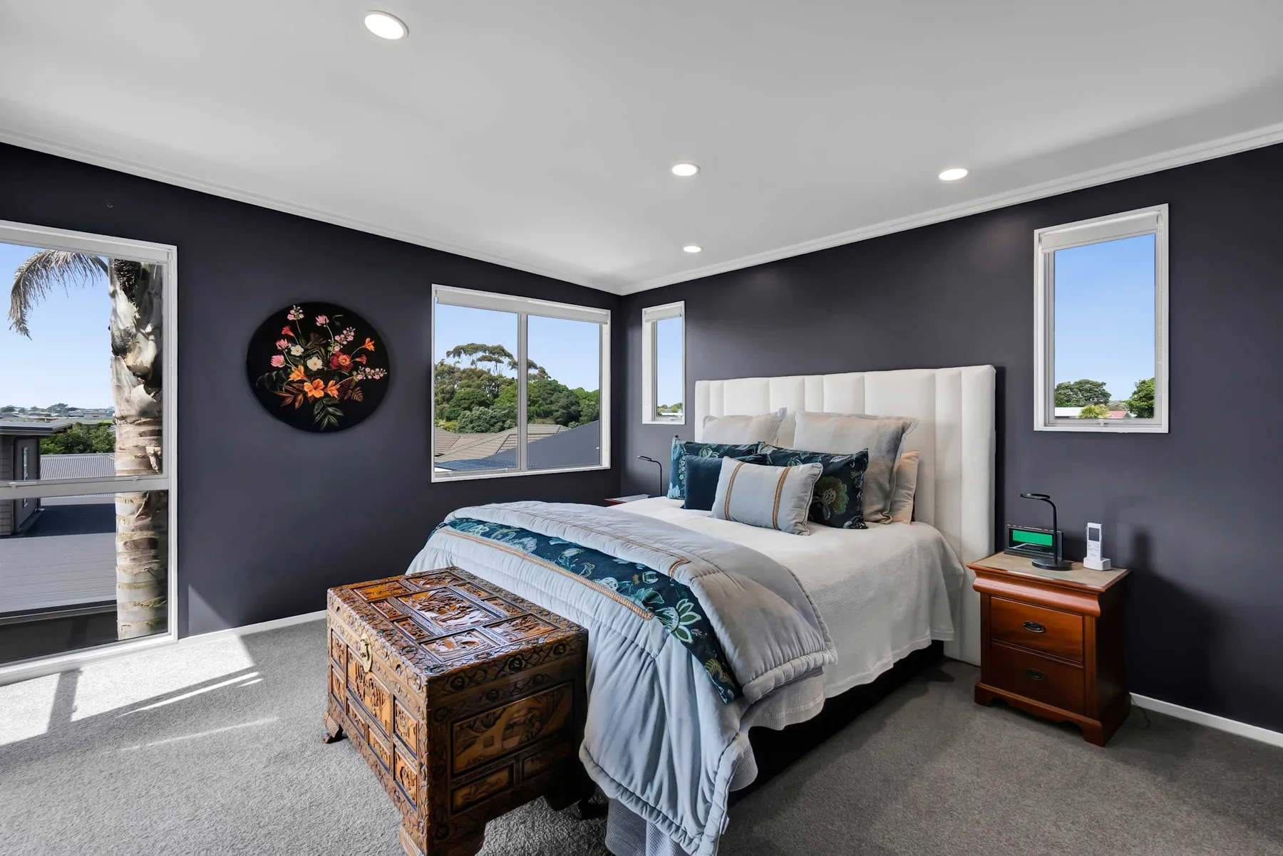 Un dormitorio con una cama grande, cojines decorativos de colores y un baúl estampado.