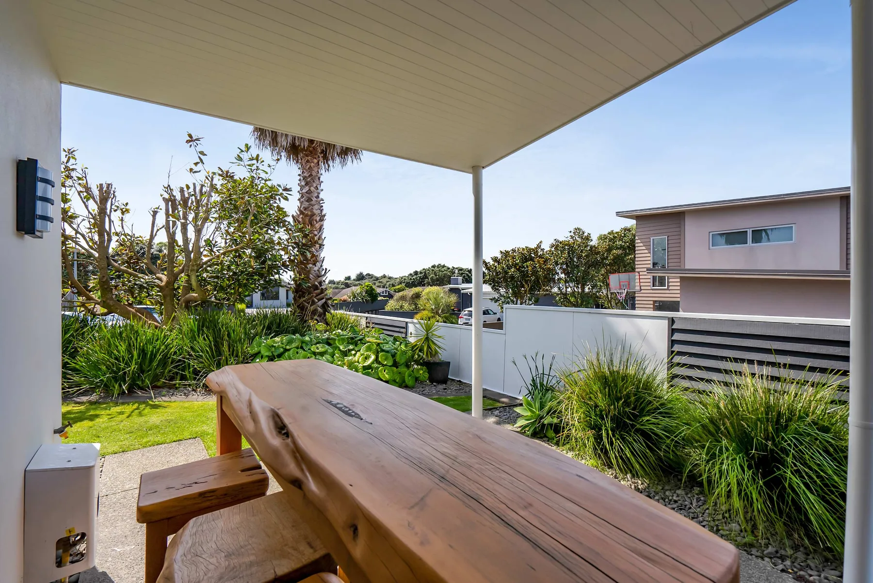 Una zona exterior cubierta con una mesa larga de madera junto a un jardín ajardinado.