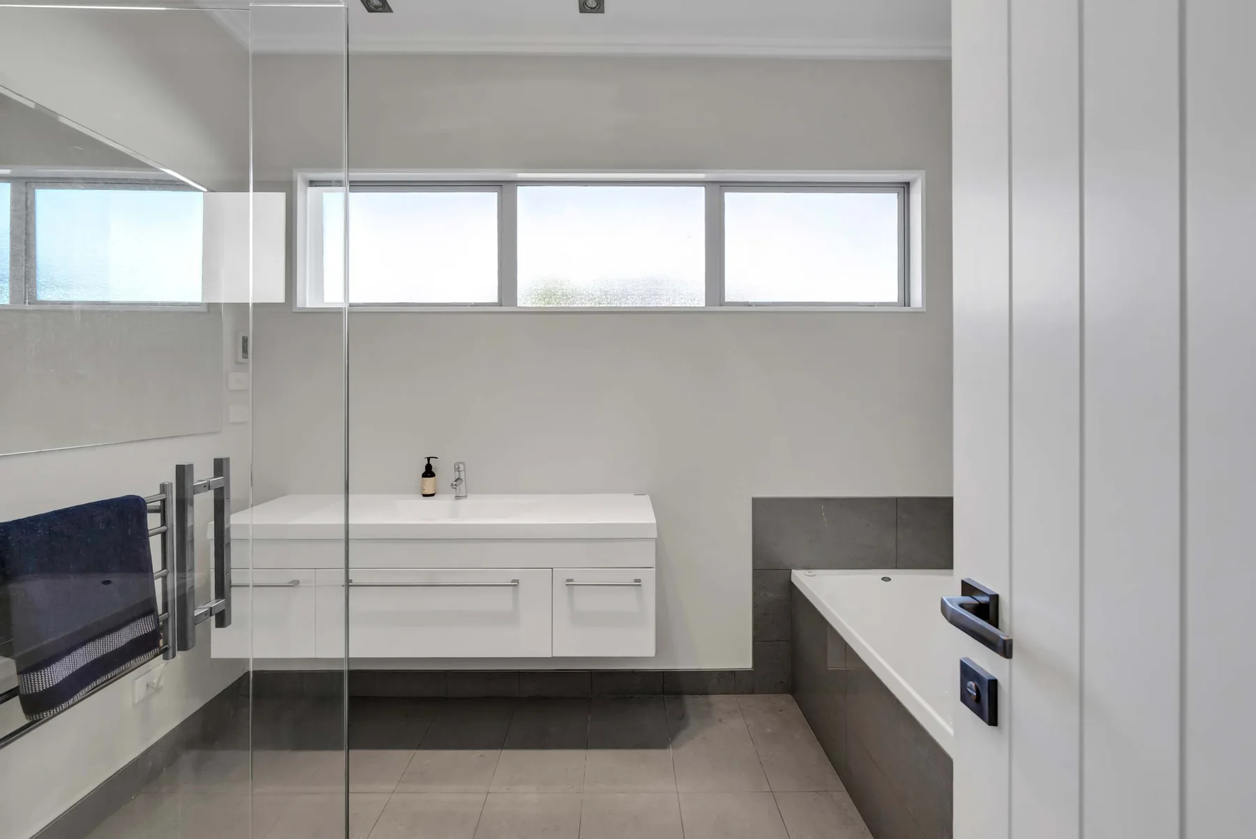 Un baño moderno con bañera, tocador y ventanas amplias.