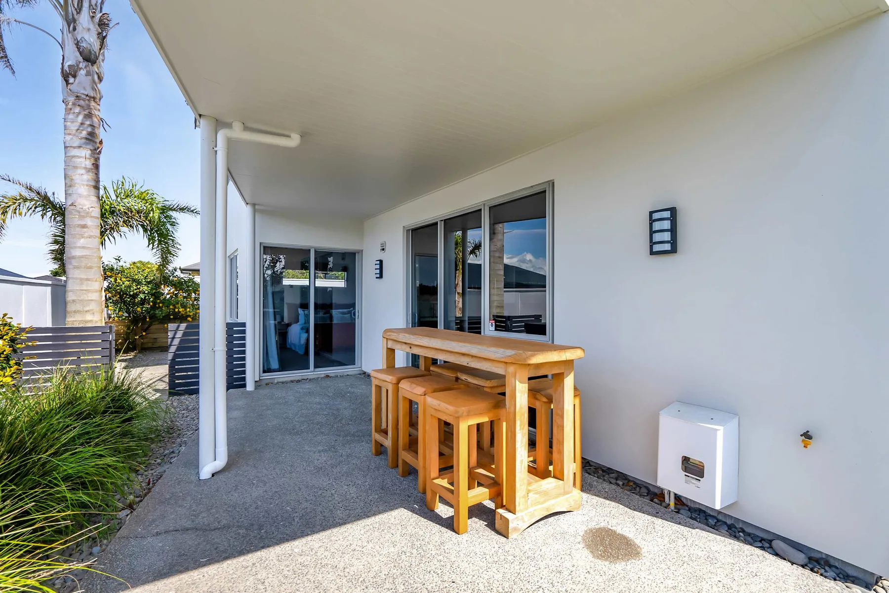 Un patio cubierto con una mesa de madera y asientos junto a puertas de vidrio.