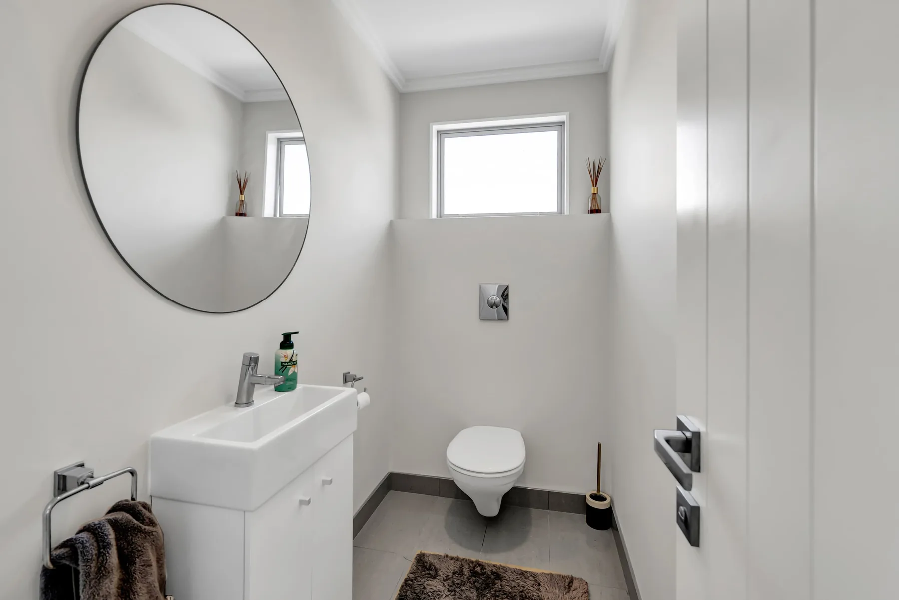 Un baño luminoso con lavabo, inodoro y espejo redondo en la pared.