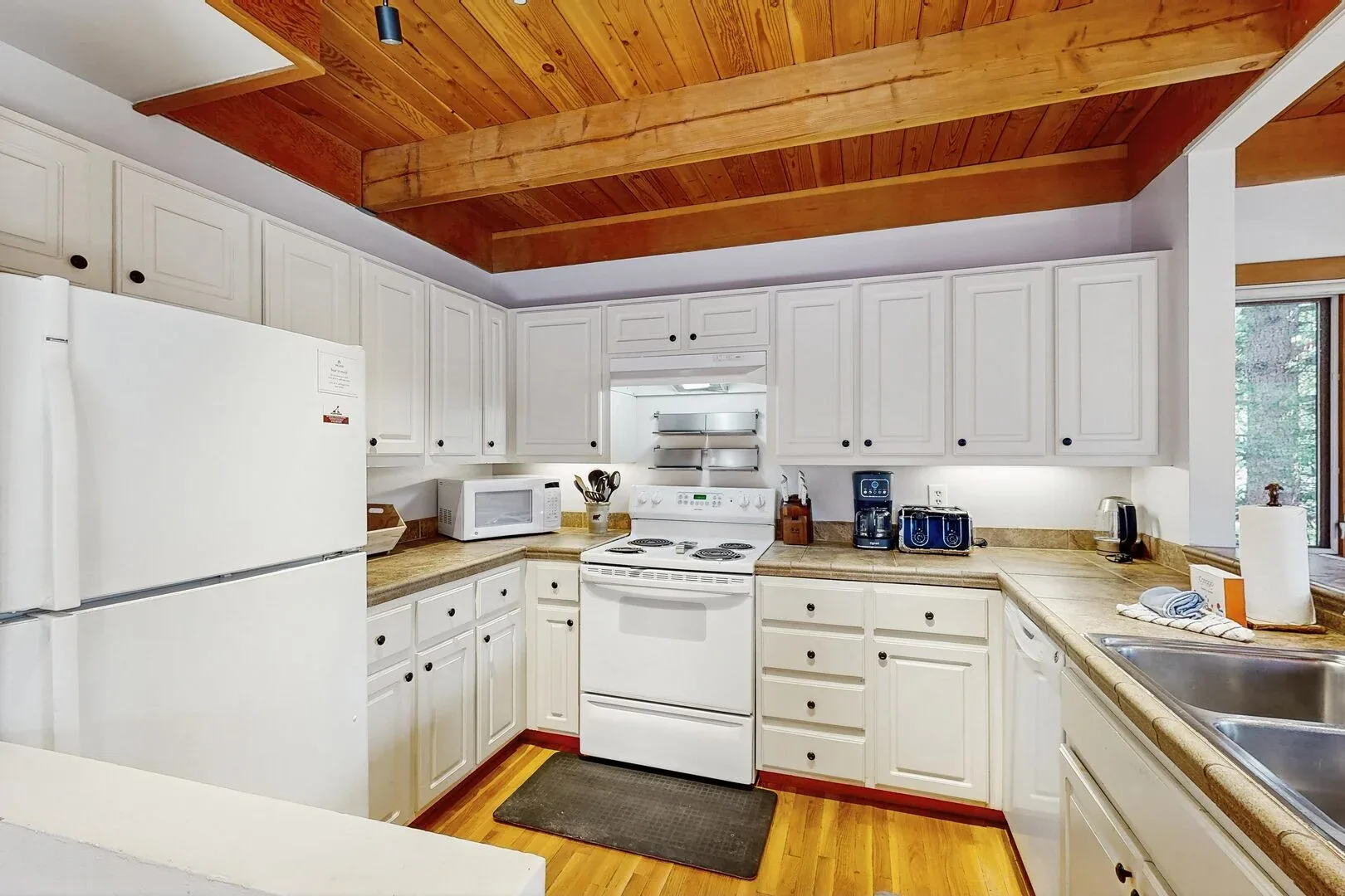 A bright kitchen with white cabinets, appliances, and a wood-paneled ceiling.
