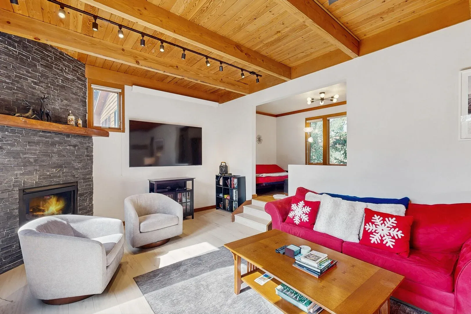 A living room with seating, a television, and a wooden coffee table beneath a timber ceiling.